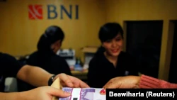 Seorang perempuan memegang uang kertas rupiah di salah satu bank keliling Bank Negara Indonesia (BNI) di Jakarta, 15 Juli 2013. (Foto: Reuters/Beawiharta)