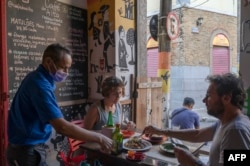 Seorang pramusaji menyajikan makanan kepada pelanggan di restoran Cafe do Alto di kawasan Lapa di Rio de Janeiro, Brazil, 24 Mei 2023. (MAURO PIMENTEL/AFP)