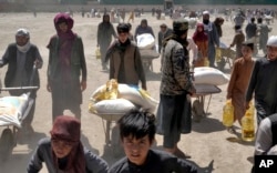 Seorang anggota Taliban berjaga ketika orang-orang menerima jatah makanan yang didistribusikan oleh kelompok bantuan kemanusiaan China, di Kabul, Afghanistan, 30 April 2022. (Foto: AP)